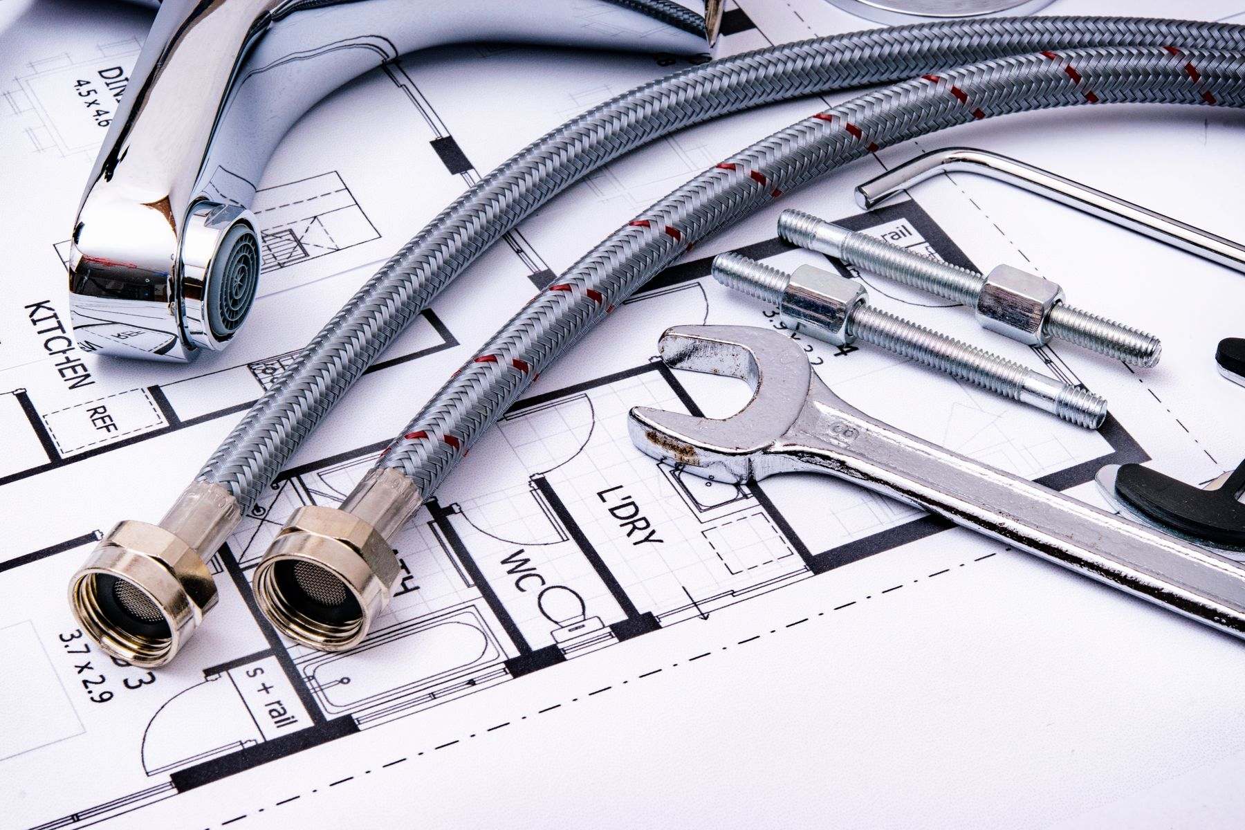 Braided supply hoses, brass fittings and a wrench laid on building plans for a new water line