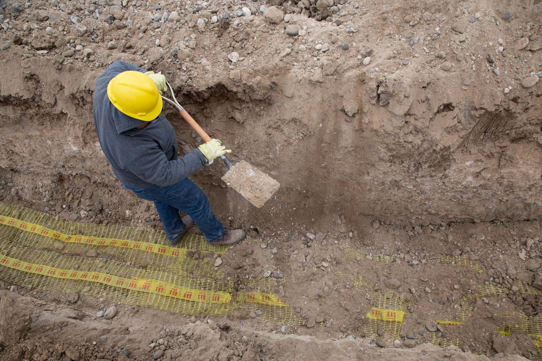 Water line repair Albany Oregon: a worker in a hard hat digs a trench down to buried pipe